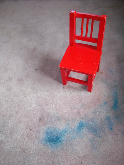 Red chair for kids on a floor with blue stains